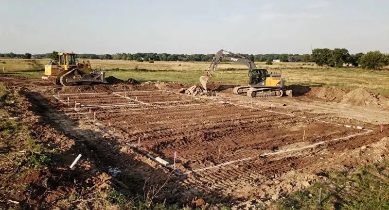 Heavy machinery doing site excavation and ground leveling for a new barndominium foundation on a rural lot.