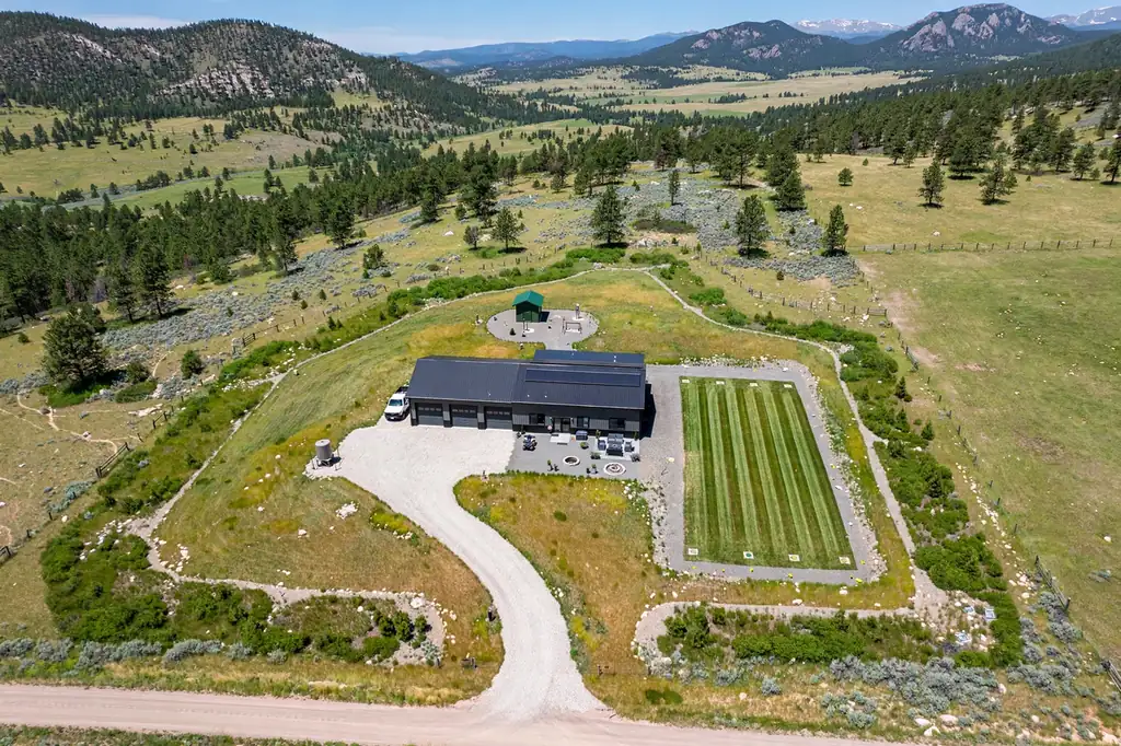 Aerial view of a finished barndominium on rural Colorado land with site prep, driveway, and mountain backdrop