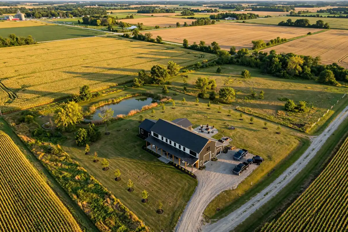 Aerial view of a finished barndominium on rural Indiana farmland with pond and long driveway
